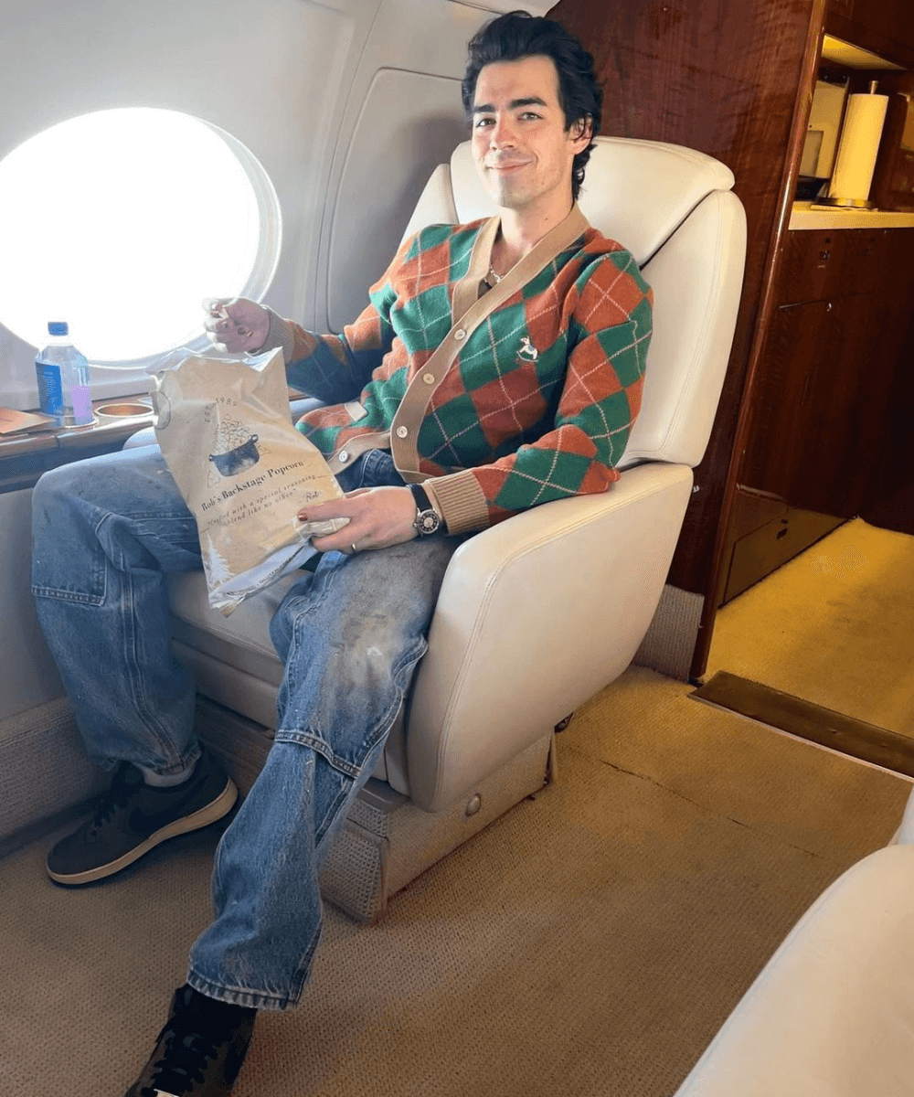 Joe Jonas - cardigan verde e laranja xadrez, calça jeans e tênis - Joe Jonas - Outono - sentado na poltrona de um avião - https://stealthelook.com.br