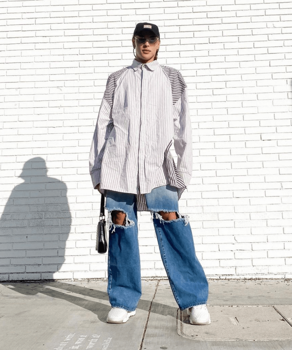Pabllo Vittar - calça jeans destroyed e camisa oversized - Lollapalooza 2022 - Outono - em pé na rua usando um boné e óculos de sol - https://stealthelook.com.br