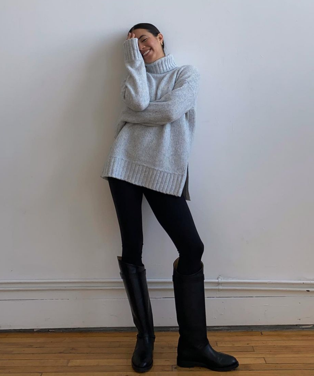 Sasha Mei - legging preta, tricot oversized de gola alta e botas - peças essenciais - Inverno - em pé na casa com uma parede de fundo branco - https://stealthelook.com.br
