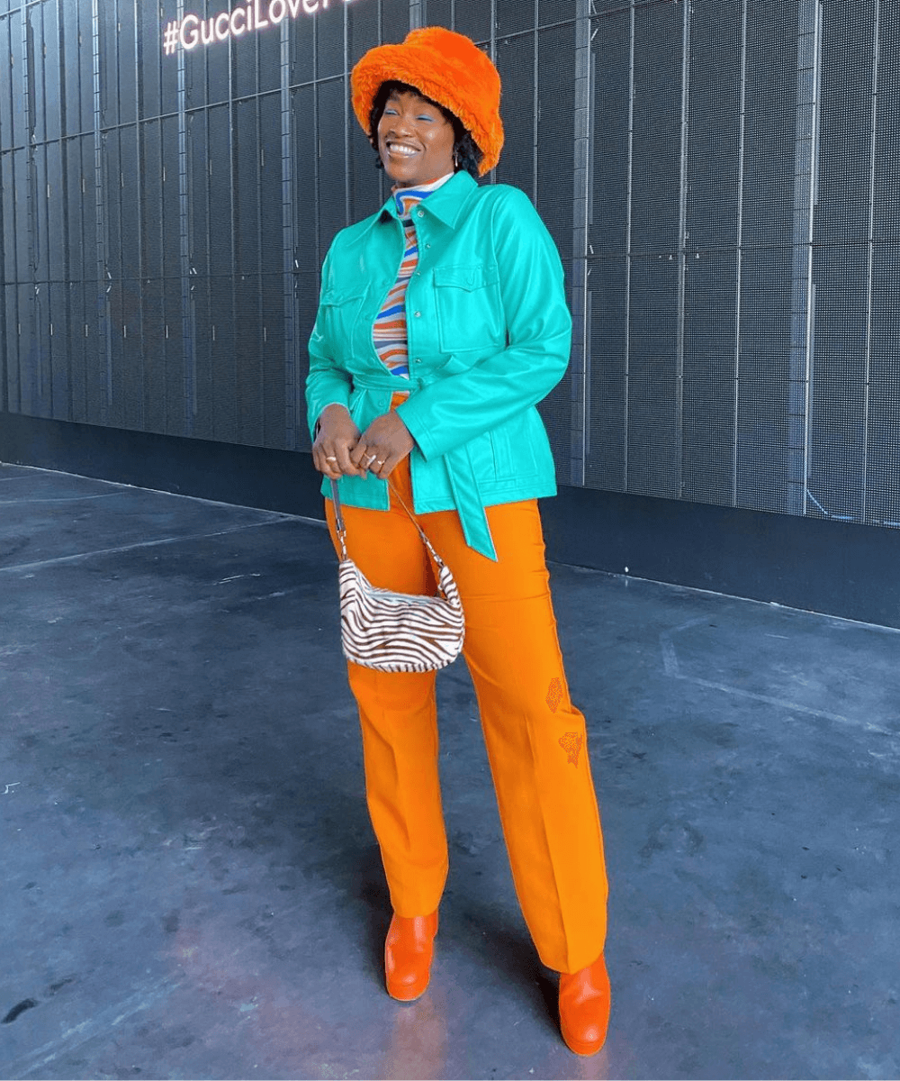 Yolande Macon - calça laranja, jaqueta azul e bucket hat de pelúcia laranja - dopamine dressing - Inverno - em pé na rua usando um chapéu laranja - https://stealthelook.com.br
