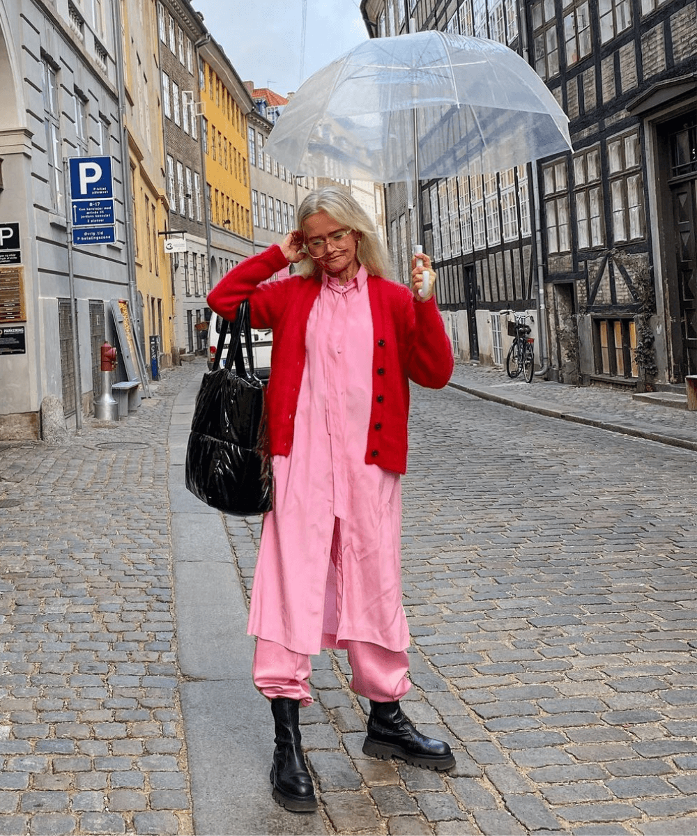 Mette | @msorrig - calça rosa, blusa rosa e casaco vermelho - dopamine dressing - Inverno  - andando na rua carregando um guarda-chuva transparente - https://stealthelook.com.br