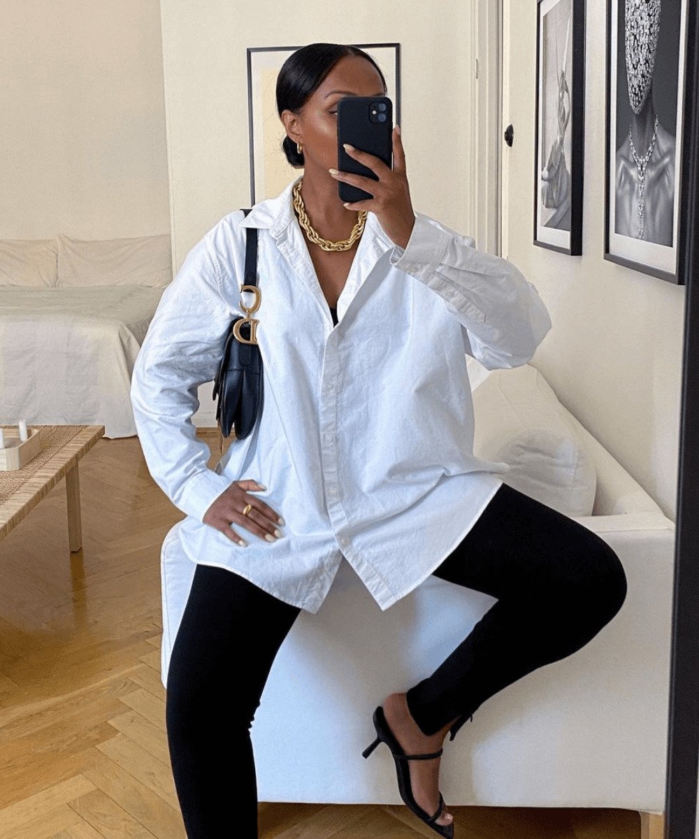 Lydia | @femmeblk - calça legging preta e camisa oversized branca - roupas de academia - Outono - sentada em um sofá com a perna direita dobrada tirando uma foto no espelho - https://stealthelook.com.br