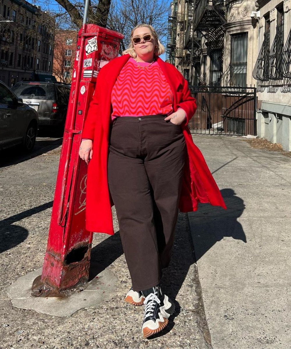 Abby Bible - calça preta, tricot rosa listrado e casaco vermelho - looks coloridos - Inverno  - em pé na rua com a mão esquerda no bolso - https://stealthelook.com.br