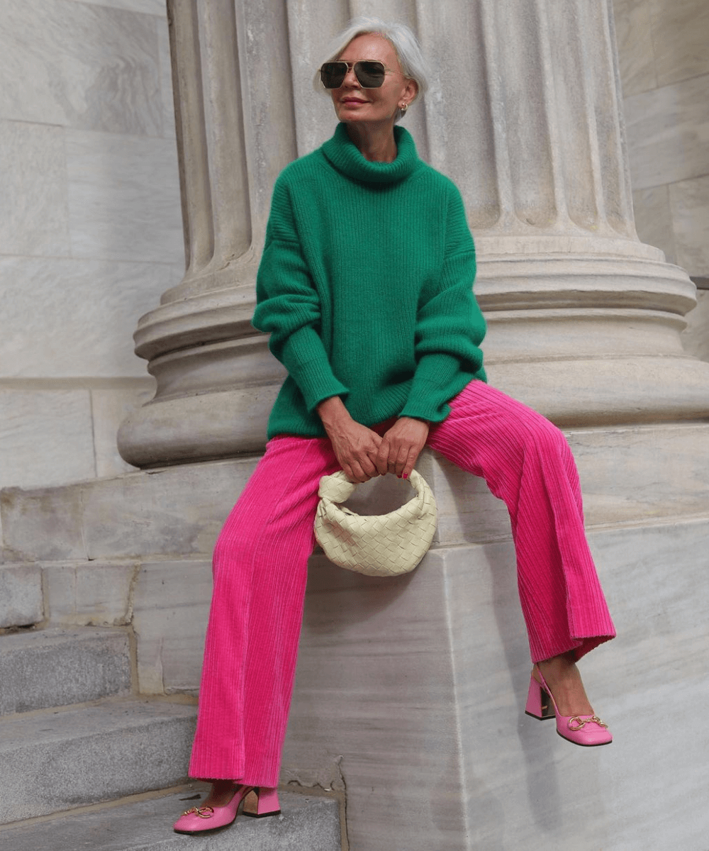 Grece Ghanem - calça rosa, tricot verde e sapato de salto quadrado rosa - sapatos confortáveis - Inverno - sentada em uma mureta, olhando para o lado e segurando uma bolsa amarela na frente do corpo - https://stealthelook.com.br