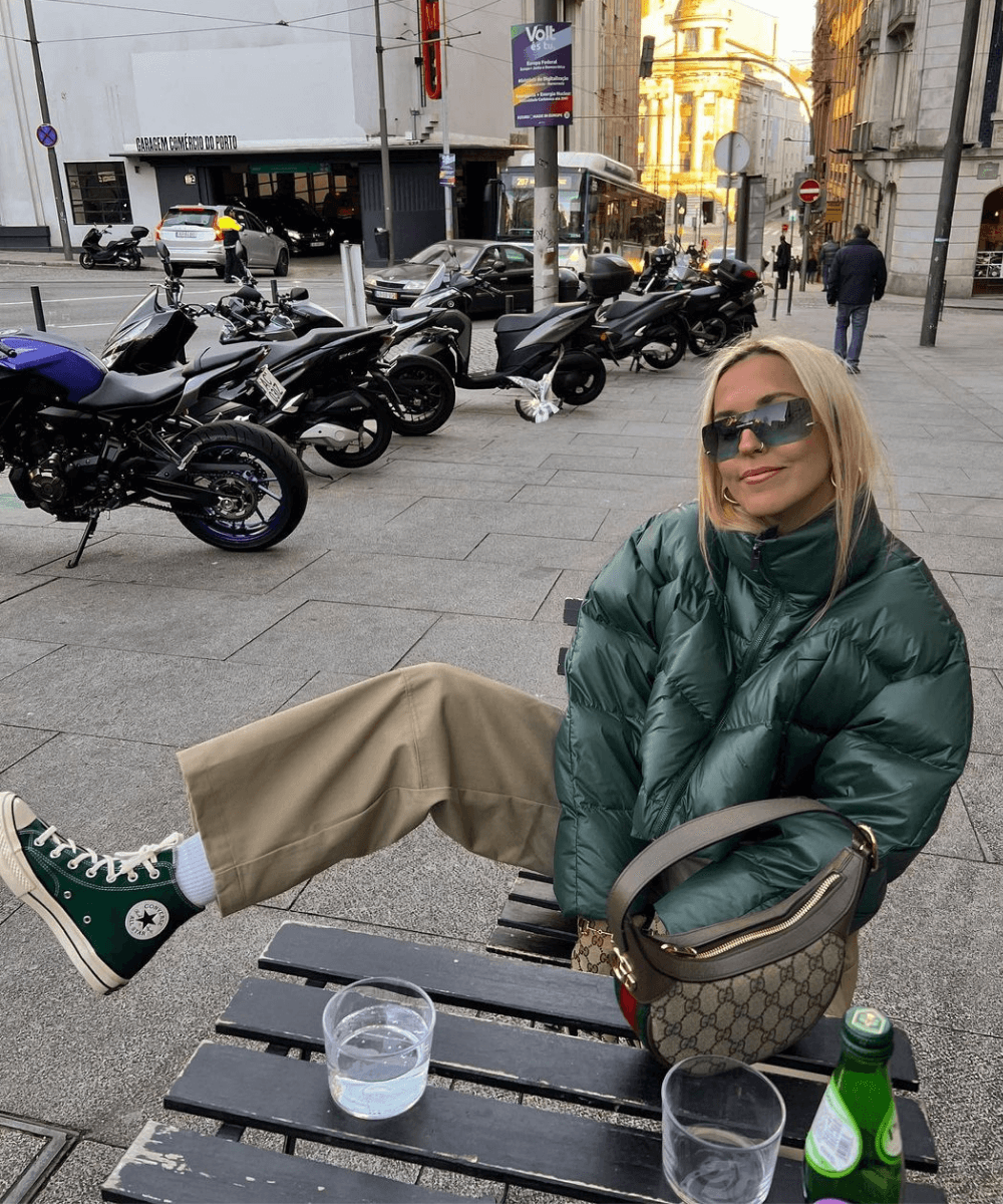 Sofia Coelho - calça bege, tênis verde e jaqueta puffer verde - tendência de moda - Inverno  - sentada em uma cadeira na rua com a perna direita flexionada - https://stealthelook.com.br