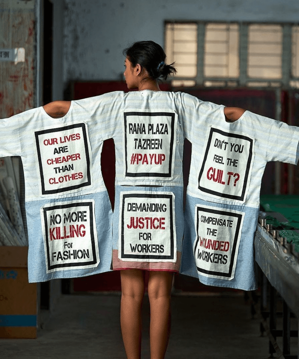 Rana Plaza - camisetas brancas estampadas com frases ativistas - Fashion Revolution Brasil - verão - menina em pé de costas com os braços abertos e camisetas penduradas - https://stealthelook.com.br