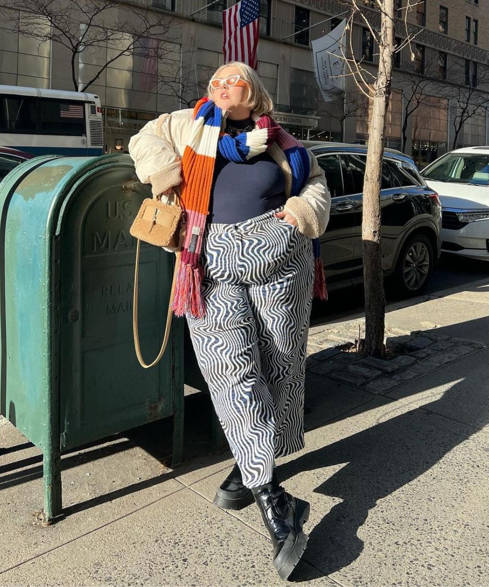 Abby Bible - calça de zebra, coturno e casaco bege com cachecol colorido - looks com coturno - Inverno  - em pé na rua encostada em uma caixa de correio verde - https://stealthelook.com.br