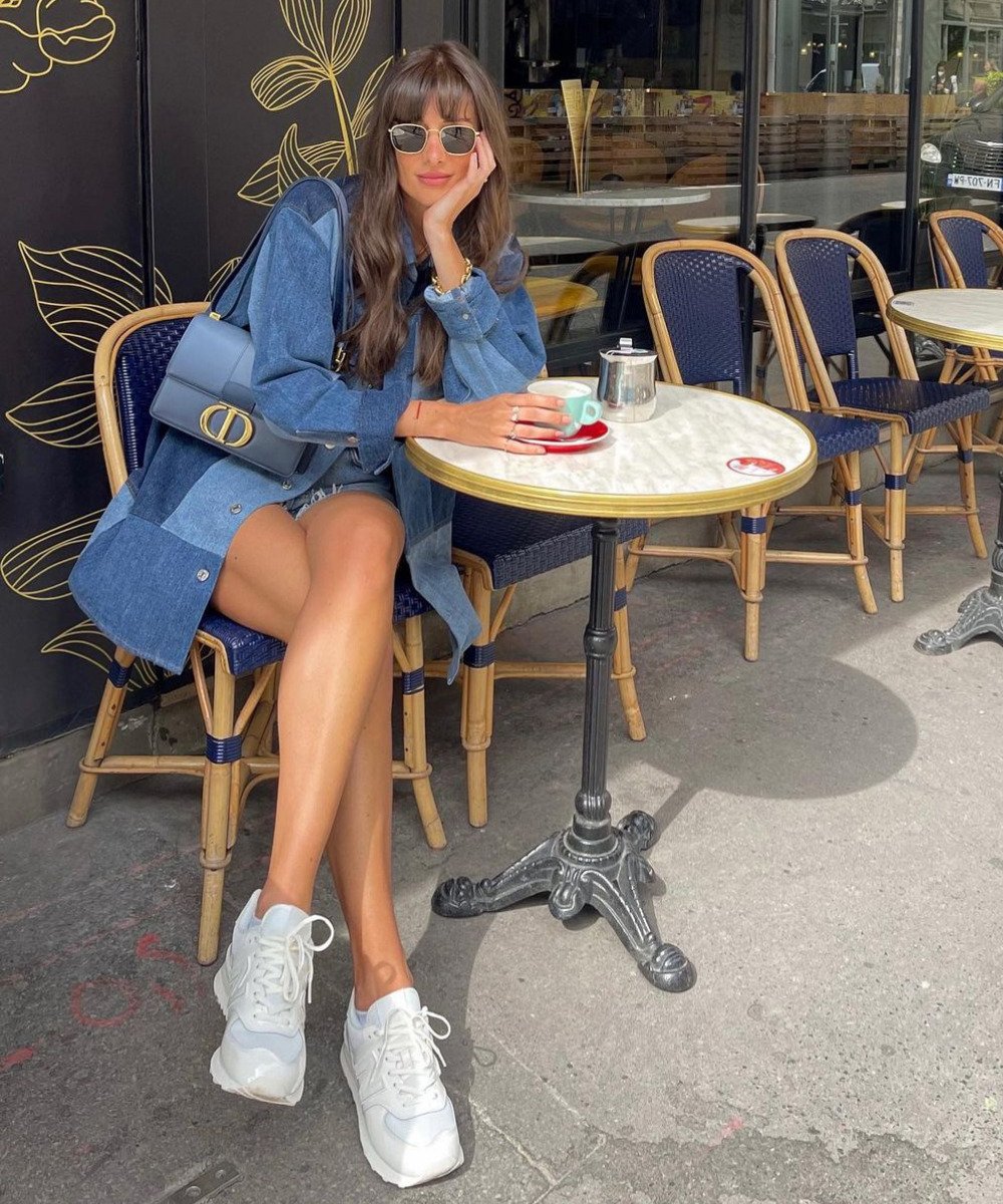 Julie Sergent Ferreri - shorts jeans, camisa jeans e tênis branco - looks jeans - Outono - sentada em uma cadeira usando óculos de sol - https://stealthelook.com.br