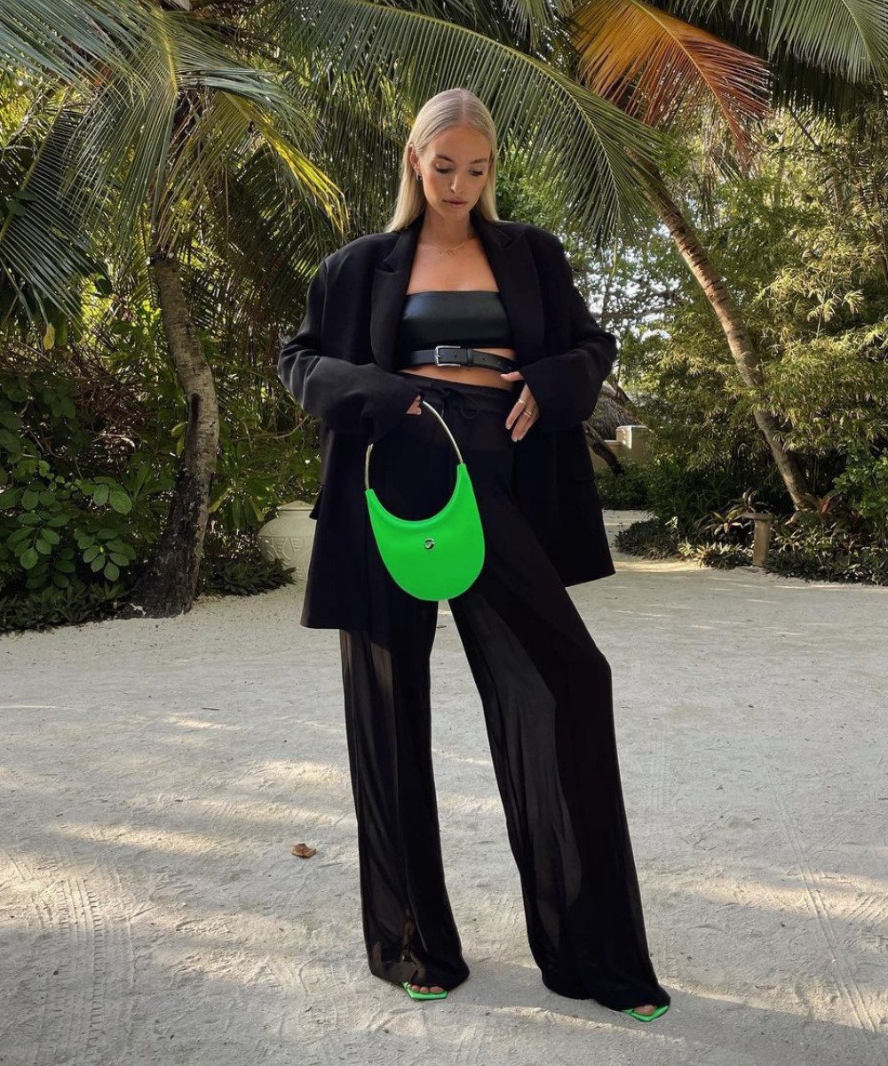 Leonie Hanne - calça transparente preta, top e blazer oversized - preto no look - Outono - em pé na rua segurando uma bolsa verde na mão - https://stealthelook.com.br