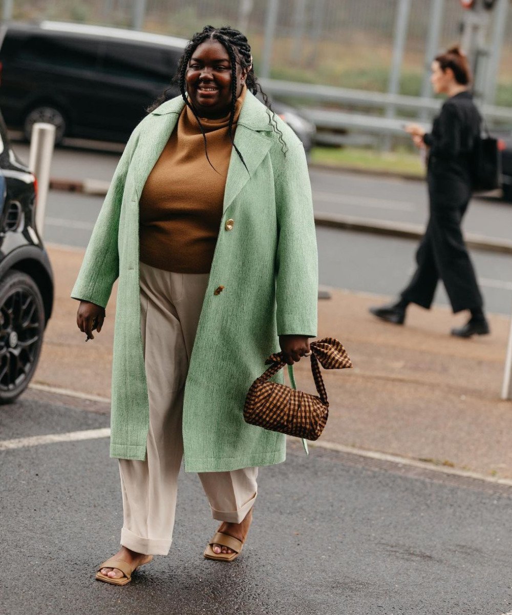 Abisola Omole - calça de alfaiataria, blusa marrom e casaco sobretudo verde menta - cores tendência - Inverno  - andando na rua segurando uma bolsa - https://stealthelook.com.br