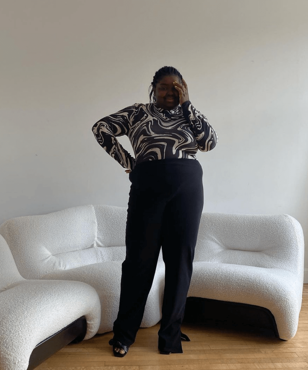 Abisola Omole - calça preta e camisa de manga longa estampada - looks novos - Outono - em pé em uma sala - https://stealthelook.com.br