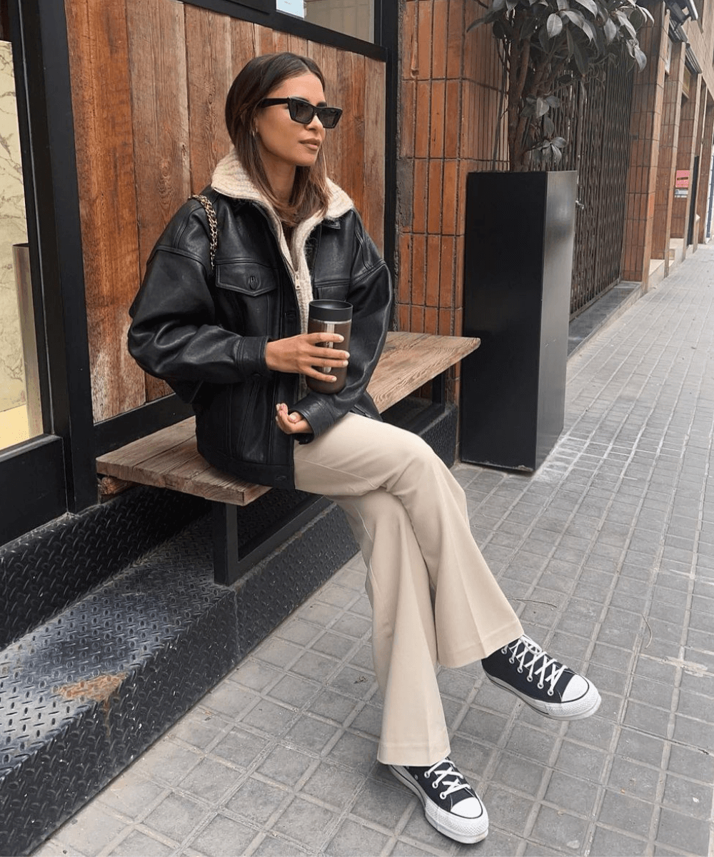Emelie Lindmark - calça bege, tricot e jaqueta preta - looks novos - Inverno  - sentada em um banco usando óculos de sol - https://stealthelook.com.br