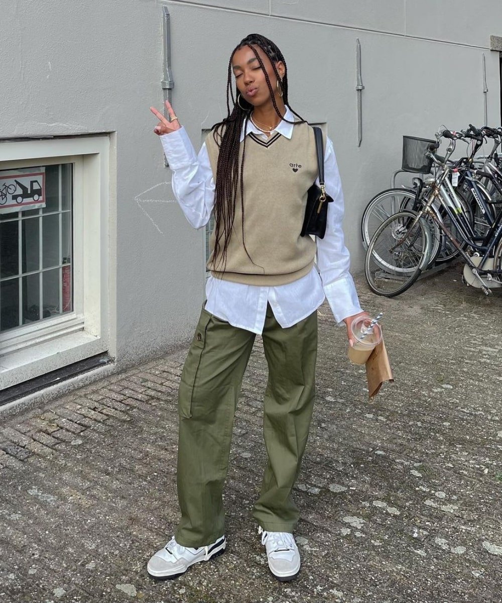 Amaka Hamelijnck - calça cargo verde, camisa e colete de tricot - inverno 2022 - Inverno - em pé na rua fazendo o sinal de 
