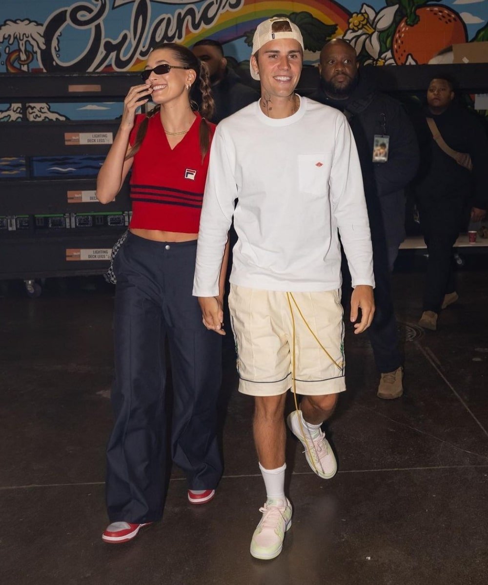 Justin e Hailey Bieber - calça azul marinho, colete vermelho e tênis branco - Hailey e Justin Bieber - Outono - em pé andando juntos - https://stealthelook.com.br