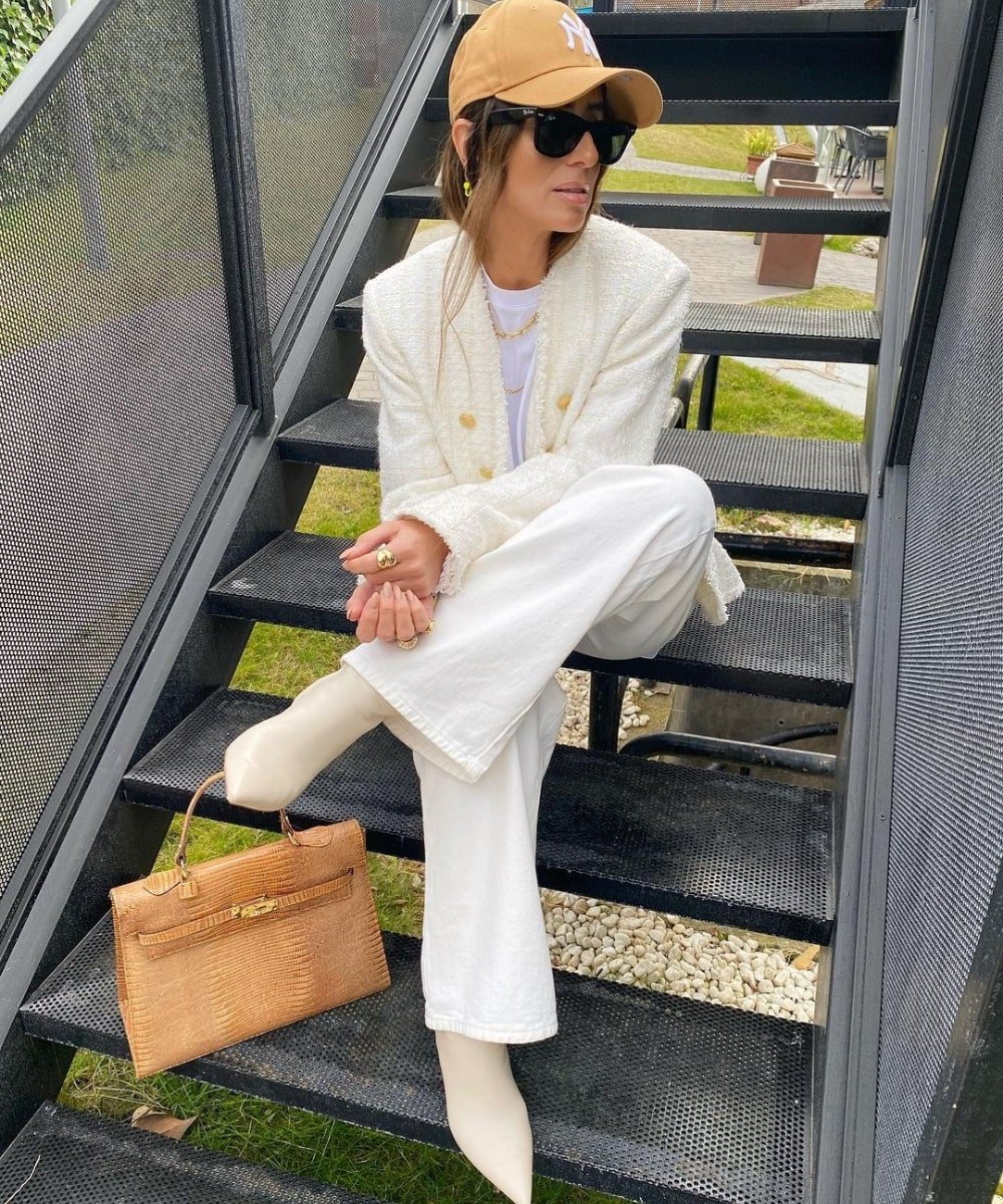 Laura Eguizabal - calça branca, blazer branco, botas de bico fino e boné - bota branca - Outono - sentada em uma escada - https://stealthelook.com.br