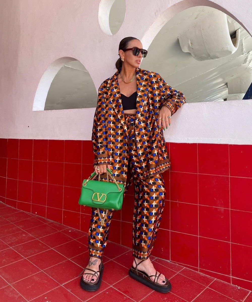 Laura Eguizabal - conjunto de calça e camisa estampada, rasteira flatform e top preto - looks novos - Verão - em pé na rua usando óculos de sol e segurando uma bolsa - https://stealthelook.com.br