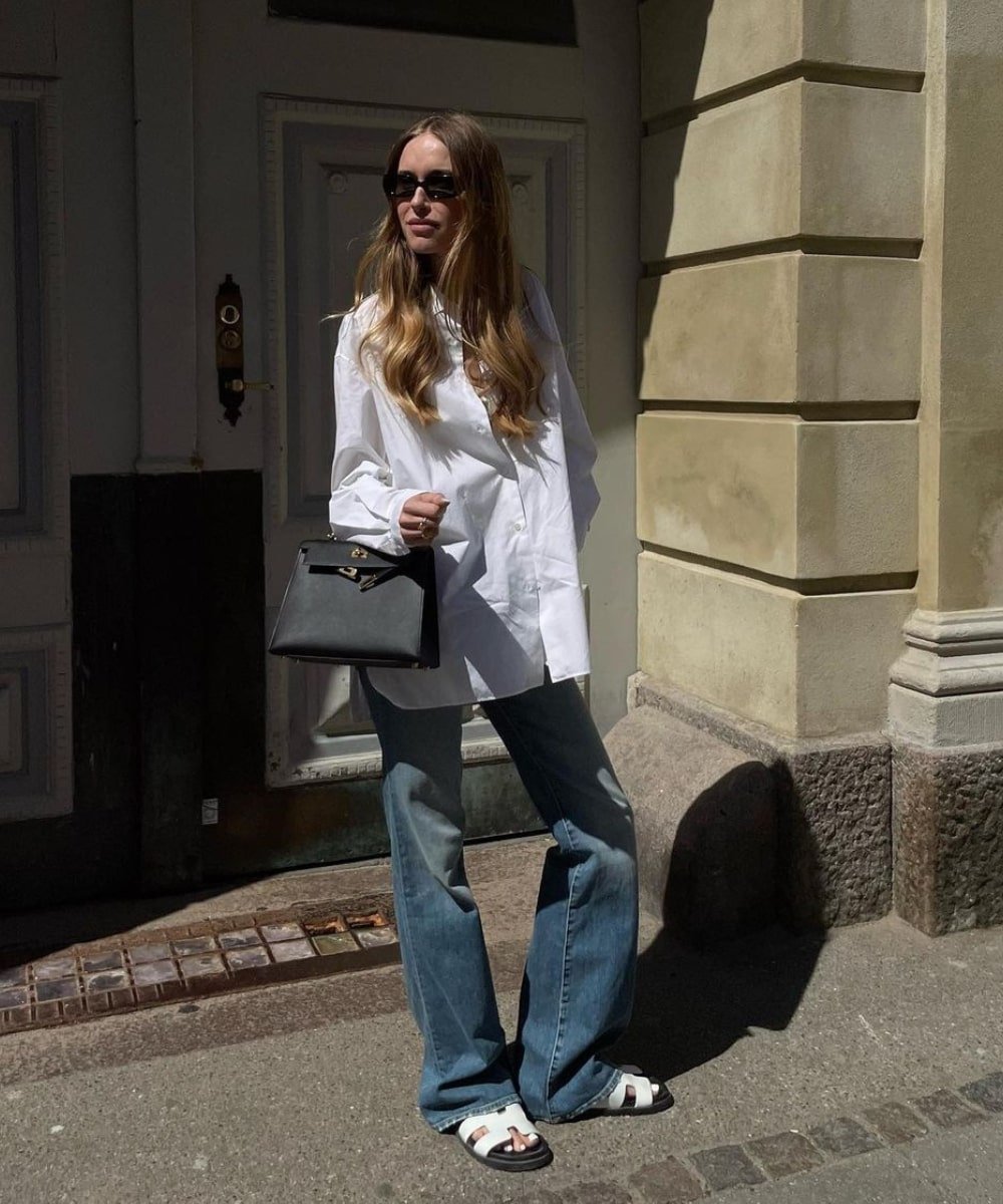 Pernille Teisbaek - calça loose jeans, camisa oversized branca e sandálias brancas - looks novos - Outono - em pé na rua usando óculos de sol - https://stealthelook.com.br