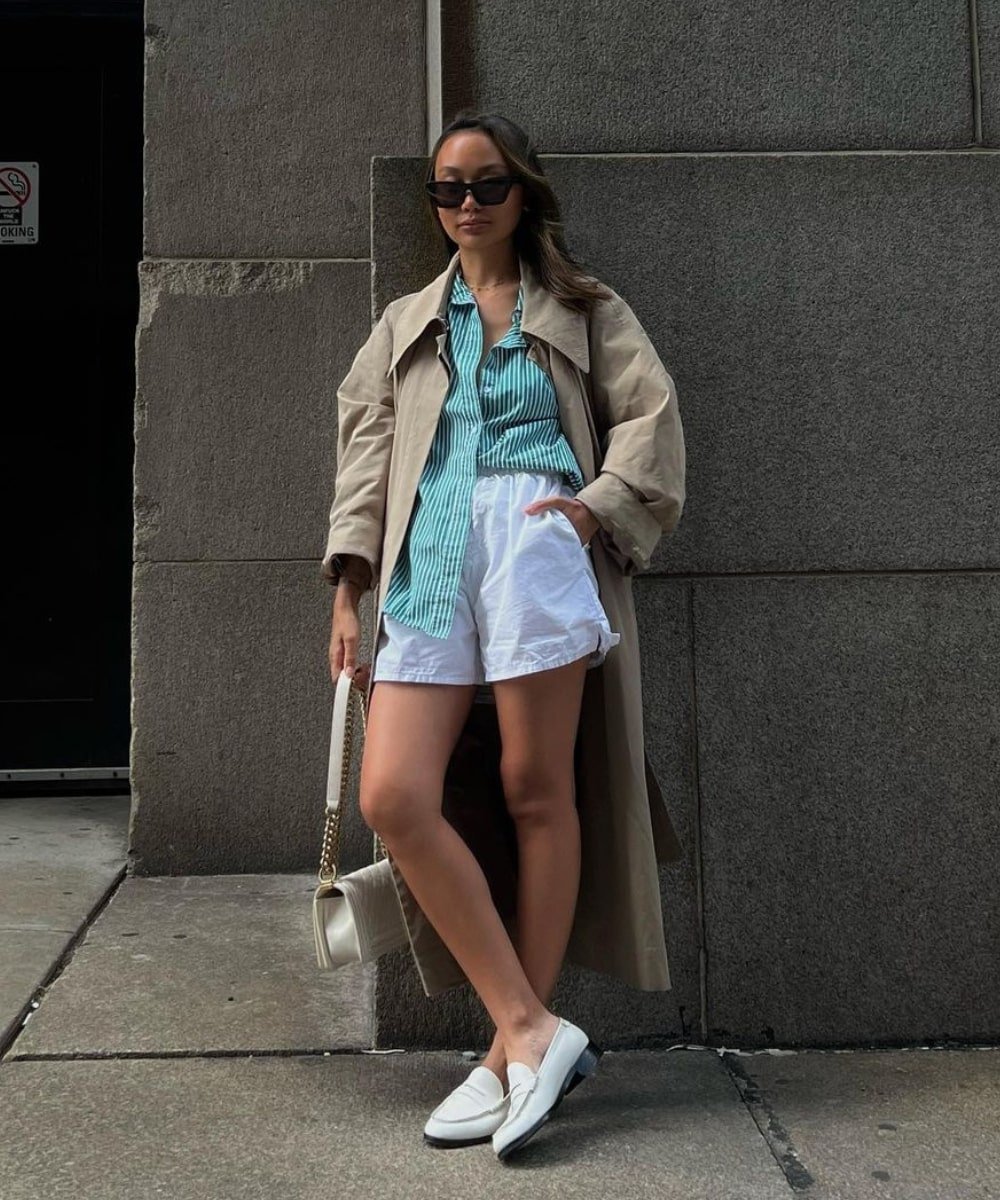 Linh Niller - shorts, camisa listrada azul e trench coat marrom - looks novos - Outono - em pé na rua - https://stealthelook.com.br
