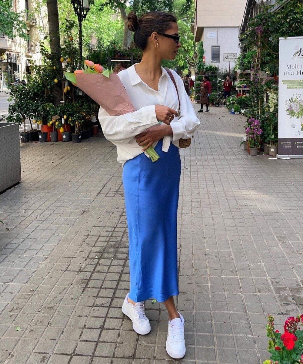 Emelie Lindmark - vestido slip dress azul, tenis e camisa branca - looks com sobreposição - Verão - em pé na rua segurando um buque de flores - https://stealthelook.com.br