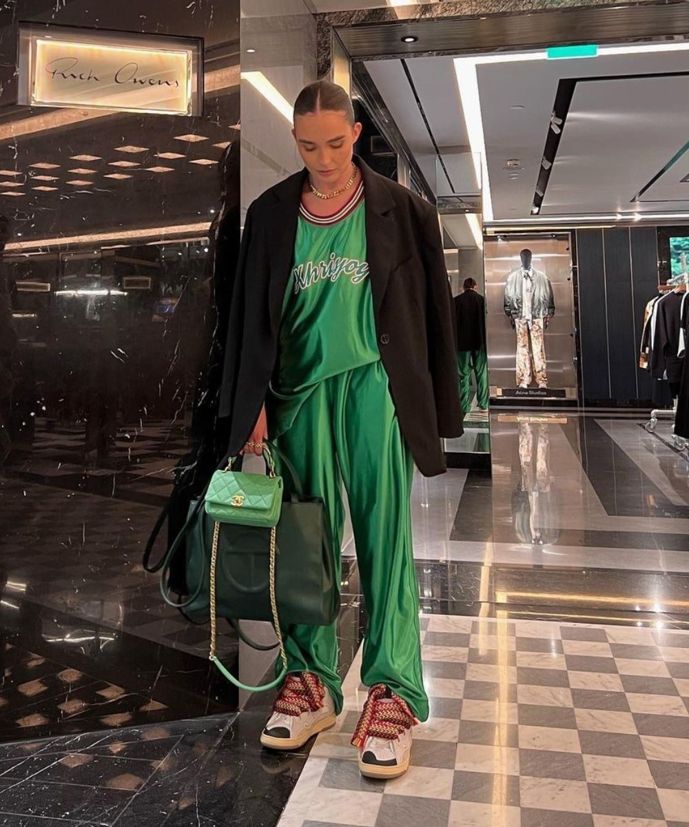 Alicia Roddy - conjunto esportivo verde, blazer preto e sapatos - Stranger Things - Inverno  - em pé em um salão - https://stealthelook.com.br