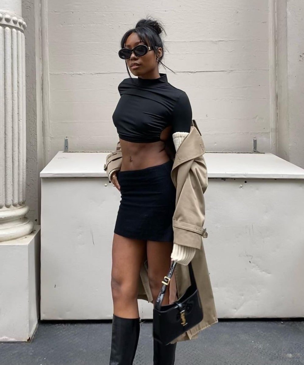 Chanel McKinsie - minissaia preta, cropped preto, trench coat e botas - looks novos - Outono - em pé na rua - https://stealthelook.com.br