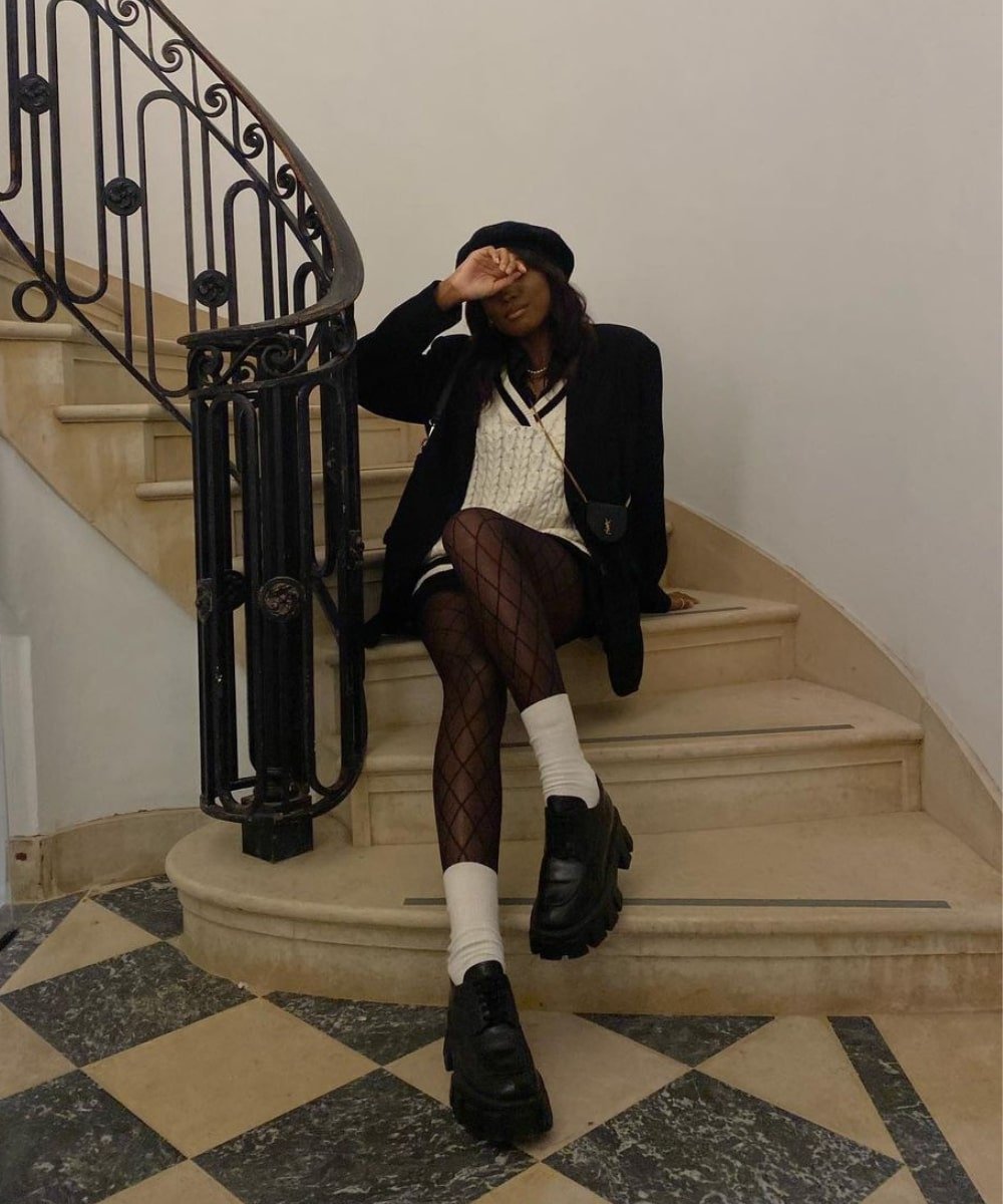 Chanel McKinsie - saia preta, meia-calça arrastão, loafer e blazer preto - Old Money - Outono - sentada em uma escada - https://stealthelook.com.br