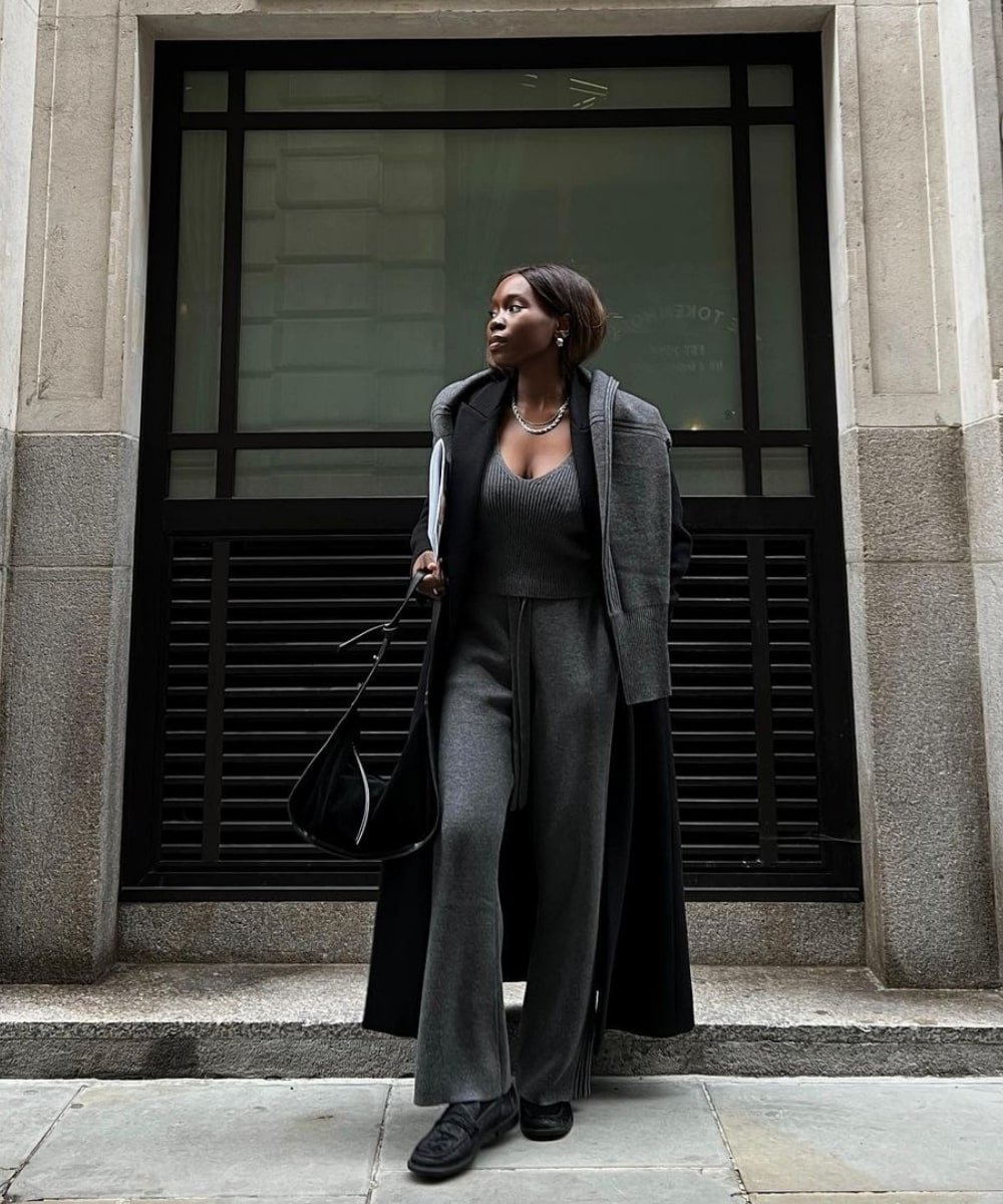 Danielle Jinadu - conjunto de trico cinza, tênis preto e casaco preto - casaco sobretudo - Inverno  - em pé na rua olhando para o lado - https://stealthelook.com.br