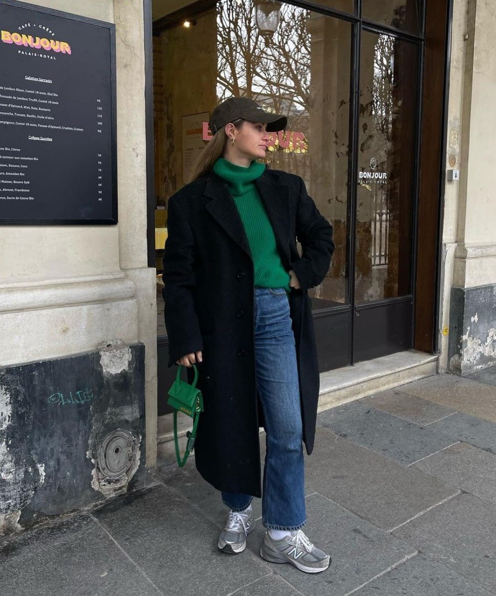 Olivia Faeh - calça jeans, trico verde de gola alta e sobretudo preto - casaco sobretudo - Inverno  - em pé na rua usando um boné - https://stealthelook.com.br