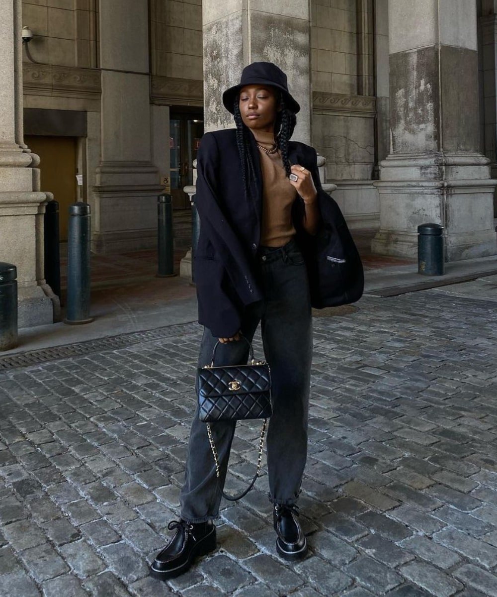 Chanel McKinsie - calça jeans, sapato oxford, tricô bege e blazer - sapato oxford - Outono - em pé na rua usando um bucket hat preto - https://stealthelook.com.br