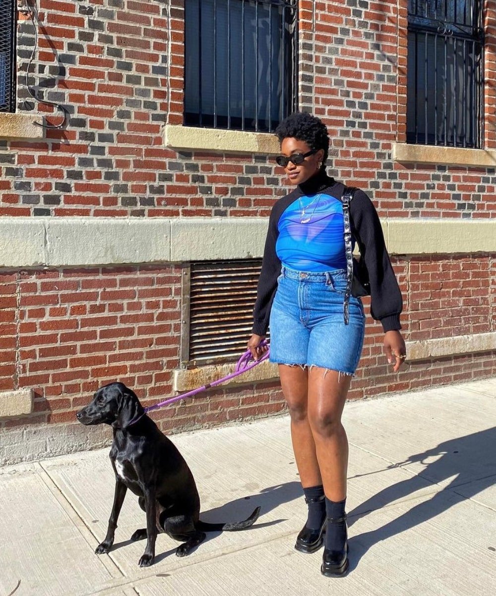 Yolande Macon - bermuda jeans, top de tule azul, tricô preto e sandália preta - look de verão - Verão - em pé na rua com um cachorro do lado - https://stealthelook.com.br