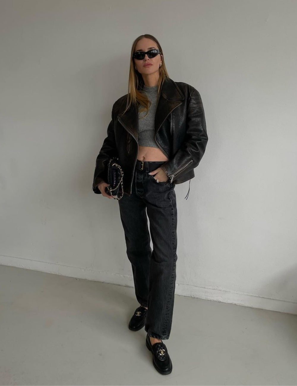 Pernille Teisbaek - calça jeans, cropped cinza, jaqueta e mocassim - looks com mocassim - Outono - em pé em uma sala usando óculos escuros - https://stealthelook.com.br