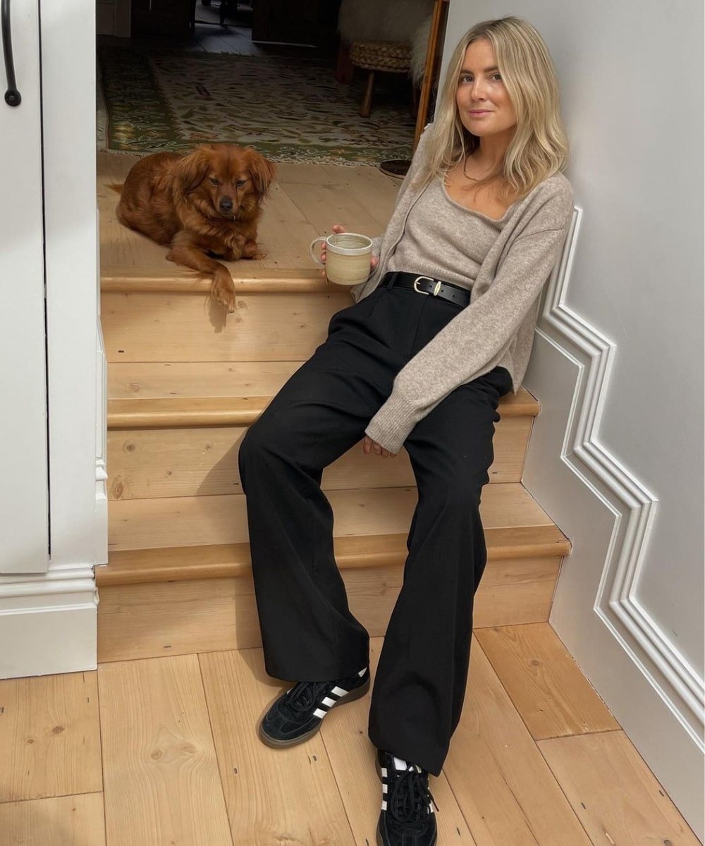 Lucy Williams - calça preta, twin set bege de tricô e tênis - Normcore - Outono - sentada em uma escada perto de um cachorro - https://stealthelook.com.br