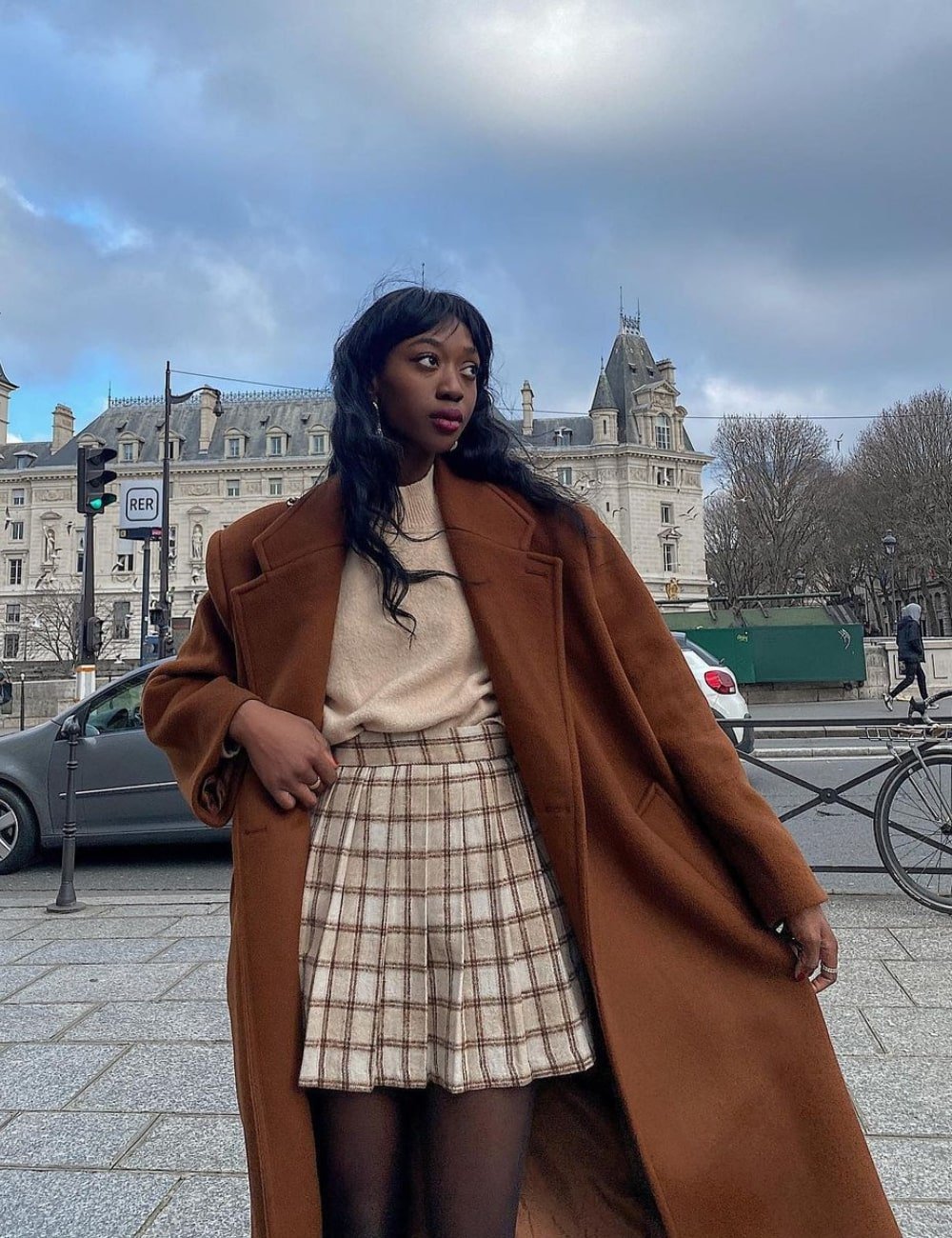 Emmanuelle Koffi - saia xadrez, tricot e sobretudo marrom - saia xadrez da Burberry - Inverno  - em pé na rua - https://stealthelook.com.br