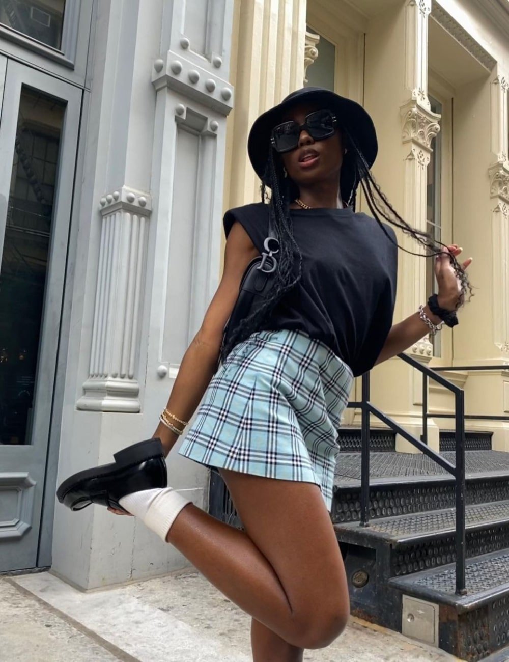 Chanel McKinsie - saia xadrez azul, blusa preta, óculos de sol e bucket hat - saia xadrez da Burberry - Verão - em pé na rua - https://stealthelook.com.br