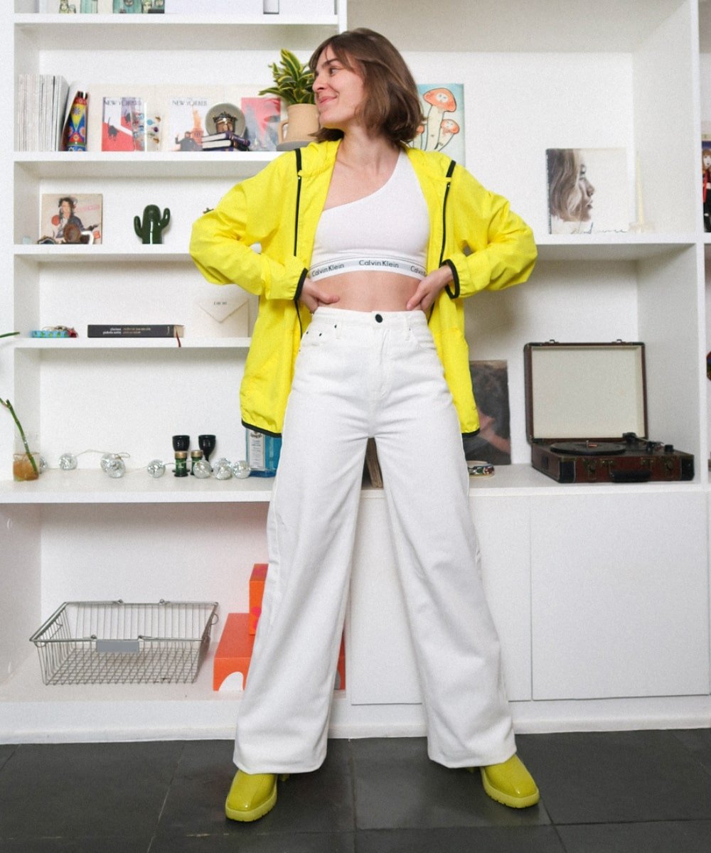 Isabela Aredes - top branco calvin klein, jaqueta amarela, calça flare e galocha - looks de festival - Verão - em pé em uma sala - https://stealthelook.com.br