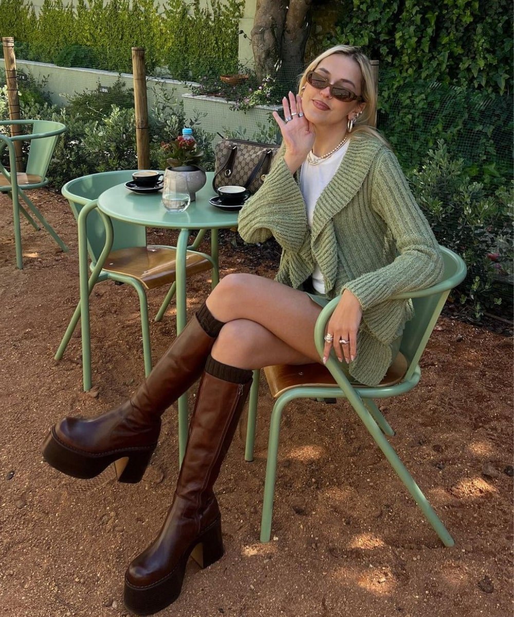 Sofia Coelho - saia, camiseta, cardiga verde e bota de plataforma marrom - modelos de botas - Outono - sentada em um café - https://stealthelook.com.br