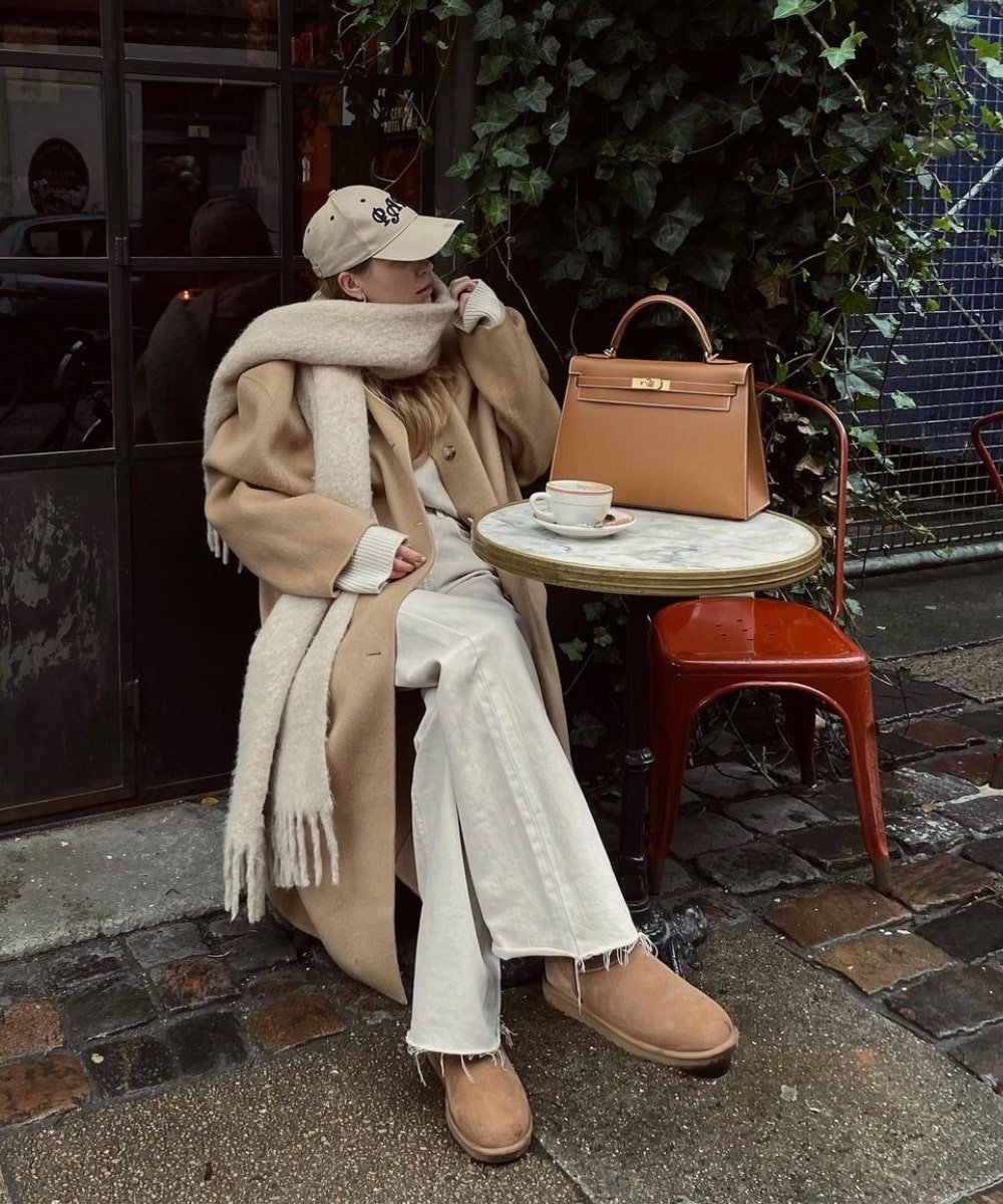 Pernille Teisbaek - calça de moletom, bota ugg, sobretudo e cachecol - modelos de botas - Inverno  - sentada em um café - https://stealthelook.com.br