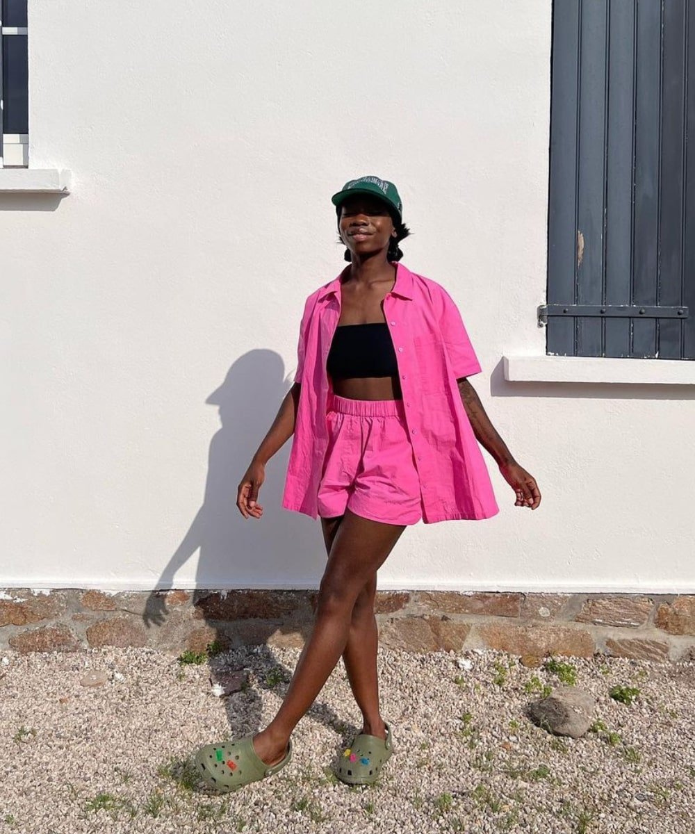Aude-Julie Alingué - conjunto rosa de shorts e camisa, crocs verde e boné - looks novos - Verão - em pé na rua - https://stealthelook.com.br