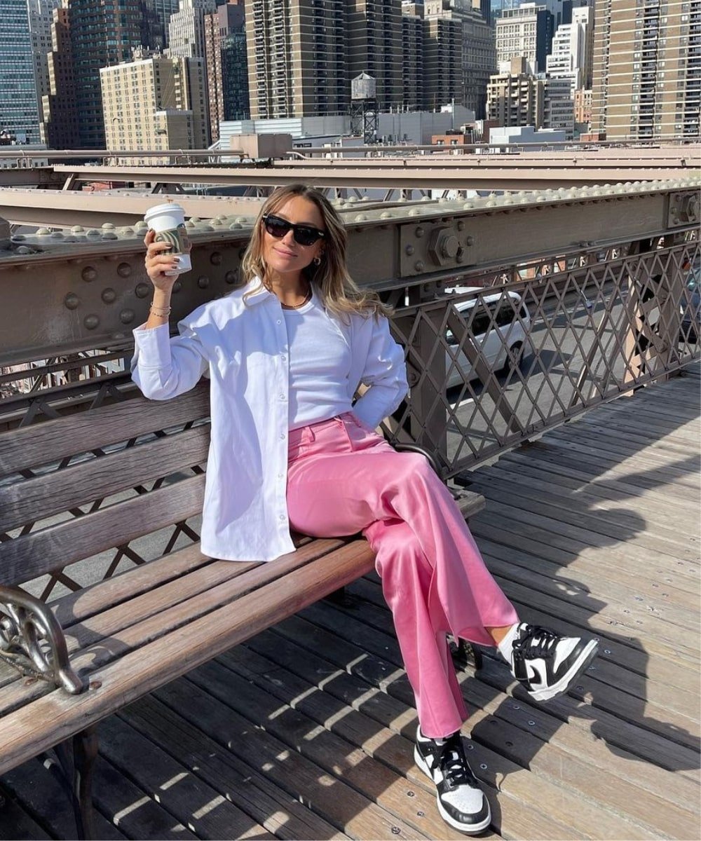 Chloé Bleinc - calça rosa, regata branca, camisa, tênis jordan preto e oculos escuros - acessórios de moda - Verão - sentada em um banco na ponte de NY - https://stealthelook.com.br