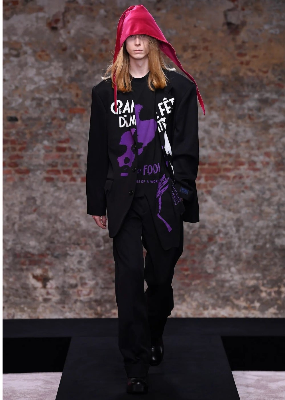 Raf Simons A/W 2022 - calça preta, tshirt estampada, blazer e chapeu rosa - London Fashion Week - Outono - modelo andando pela passarela - https://stealthelook.com.br