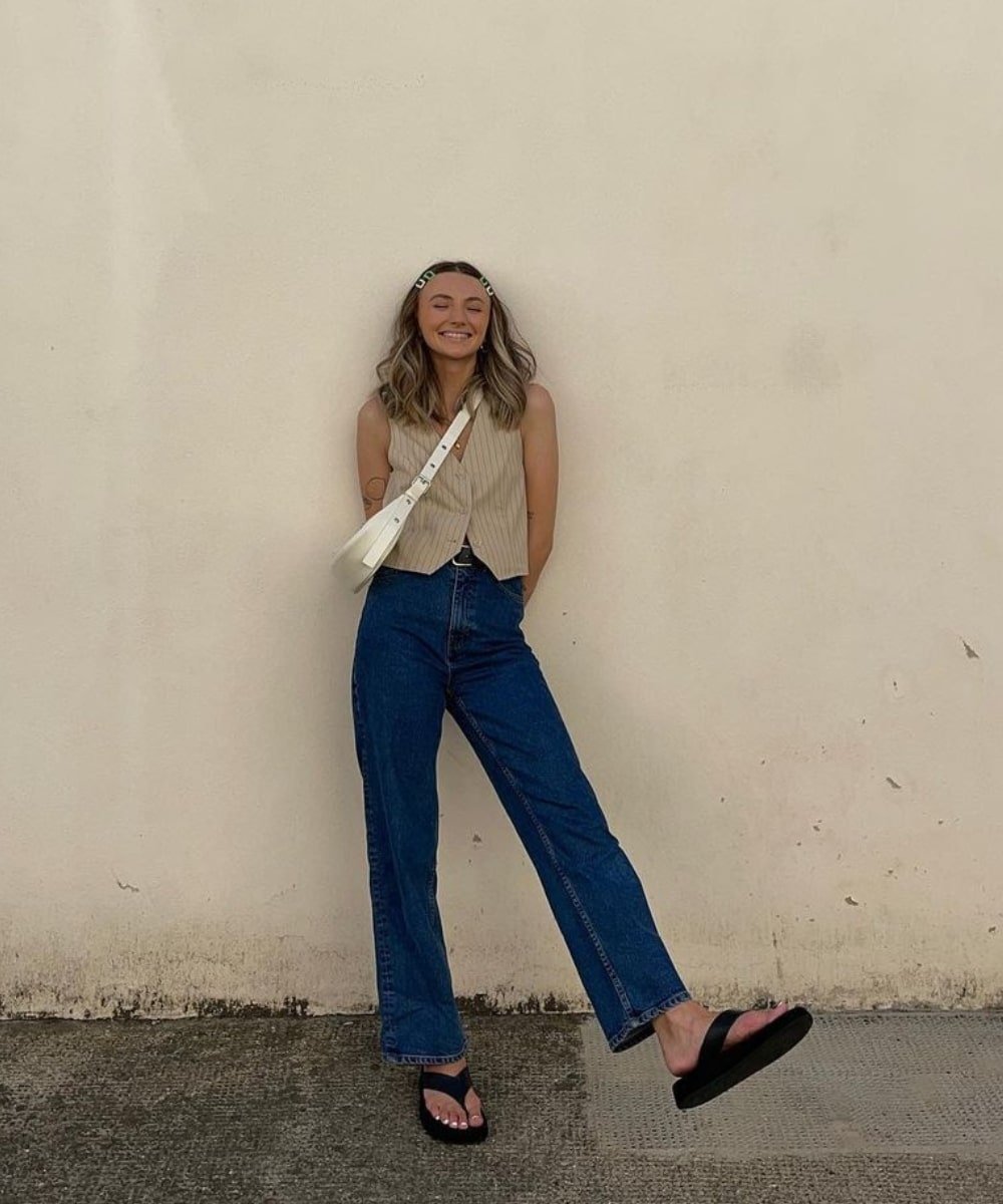 Chloe Hayward - calça jeans, colete de alfaiataria e chinelo preto - looks com chinelo - Primavera - em pé na rua - https://stealthelook.com.br