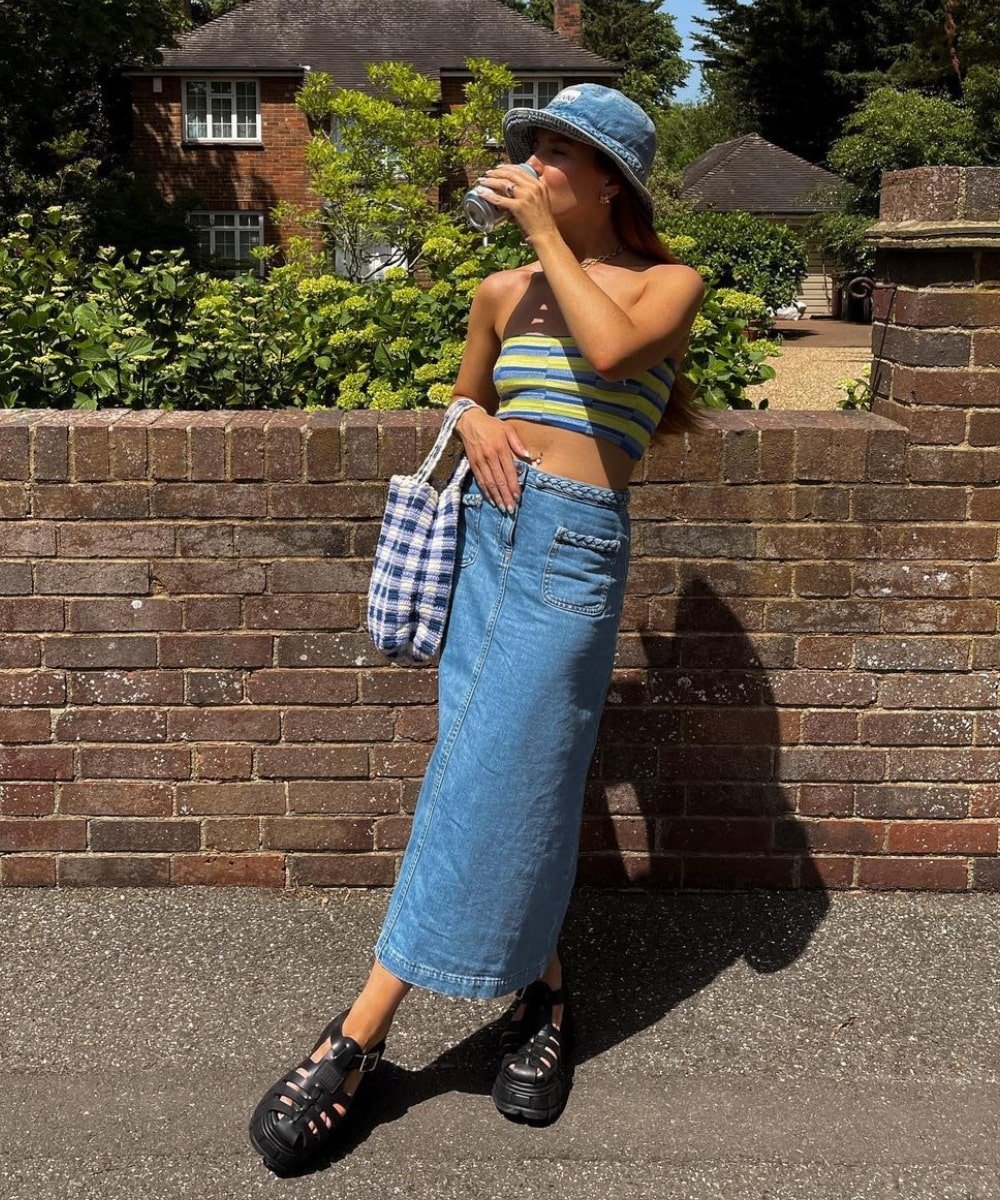 Rebecca Olivia | @rebeccaferrazwyatt - saia midi jeans, top sem alças, bucket hat azul e rasteira - looks de verão - Verão - em pé na rua - https://stealthelook.com.br