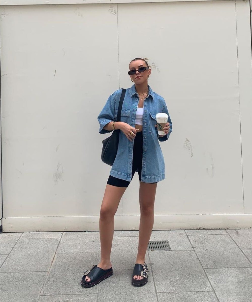 @missjamiefirth - biker shorts, regata branca, camisa jeans e rasteira - looks de verão - Verão - em pé na rua usando óculos de sol - https://stealthelook.com.br