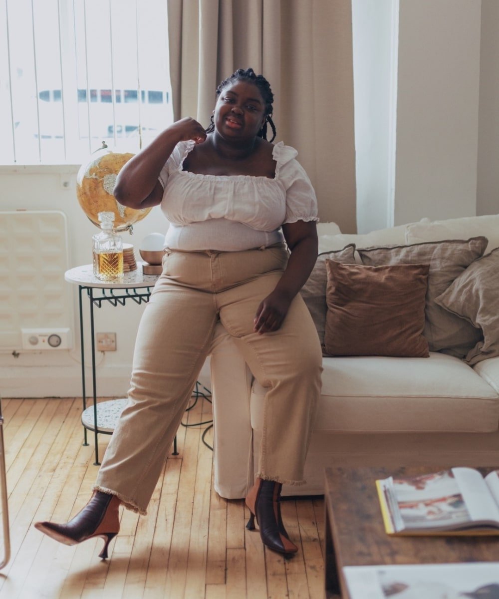 Abisola Omole - calça bege, blusa ciganinha e botas - blusa tendência - Primavera - sentada em um sofá - https://stealthelook.com.br