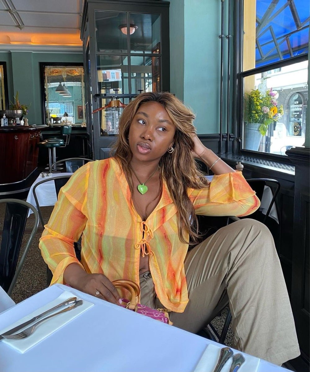 Nnenna Echem - calça verde sarja, bata laranja transparente e tenis - verão 2023 - Verão - sentada em um café - https://stealthelook.com.br