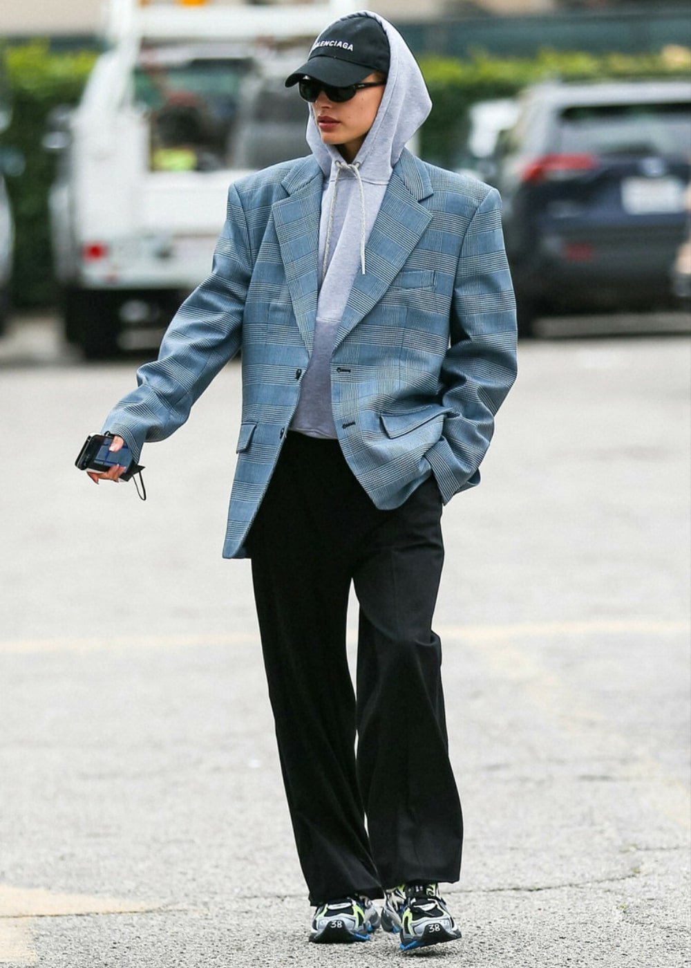 Hailey Bieber - calça jeans, moletom cinza e blazer oversized - look de aeroporto - Inverno  - andando na rua usando óculos de sol e um boné - https://stealthelook.com.br