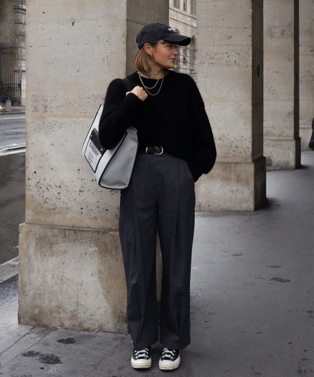 Millie Holmes - calça preta, trico preto, bone e tenis converse - looks com cinto - Outono - em pé na rua usando boné e olhando para o lado - https://stealthelook.com.br