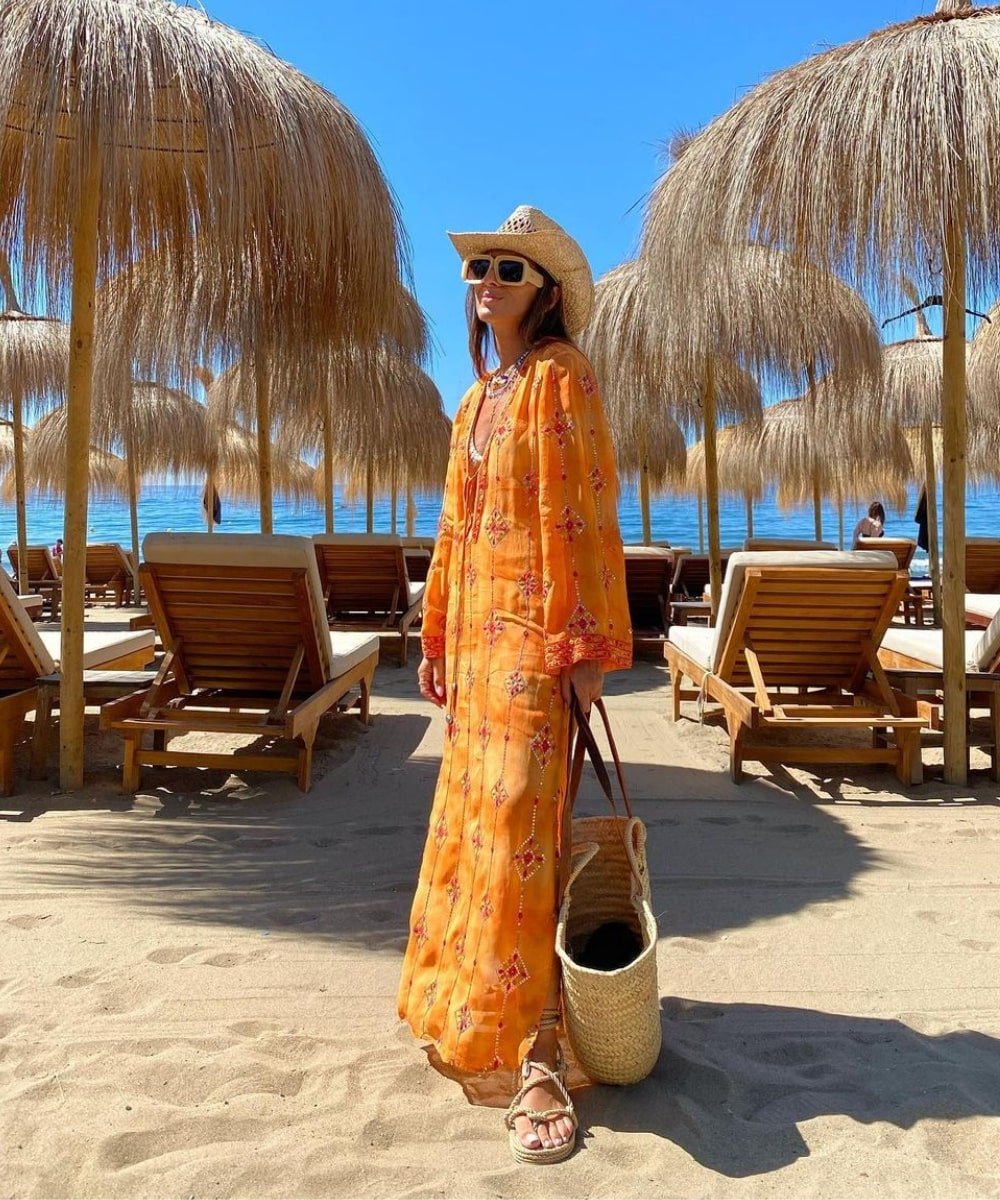 Laura Eguizabal - vestido laranja, biquini e rasteirinha - looks de praia - Verão - em pé na praia usando óculos de sol - https://stealthelook.com.br