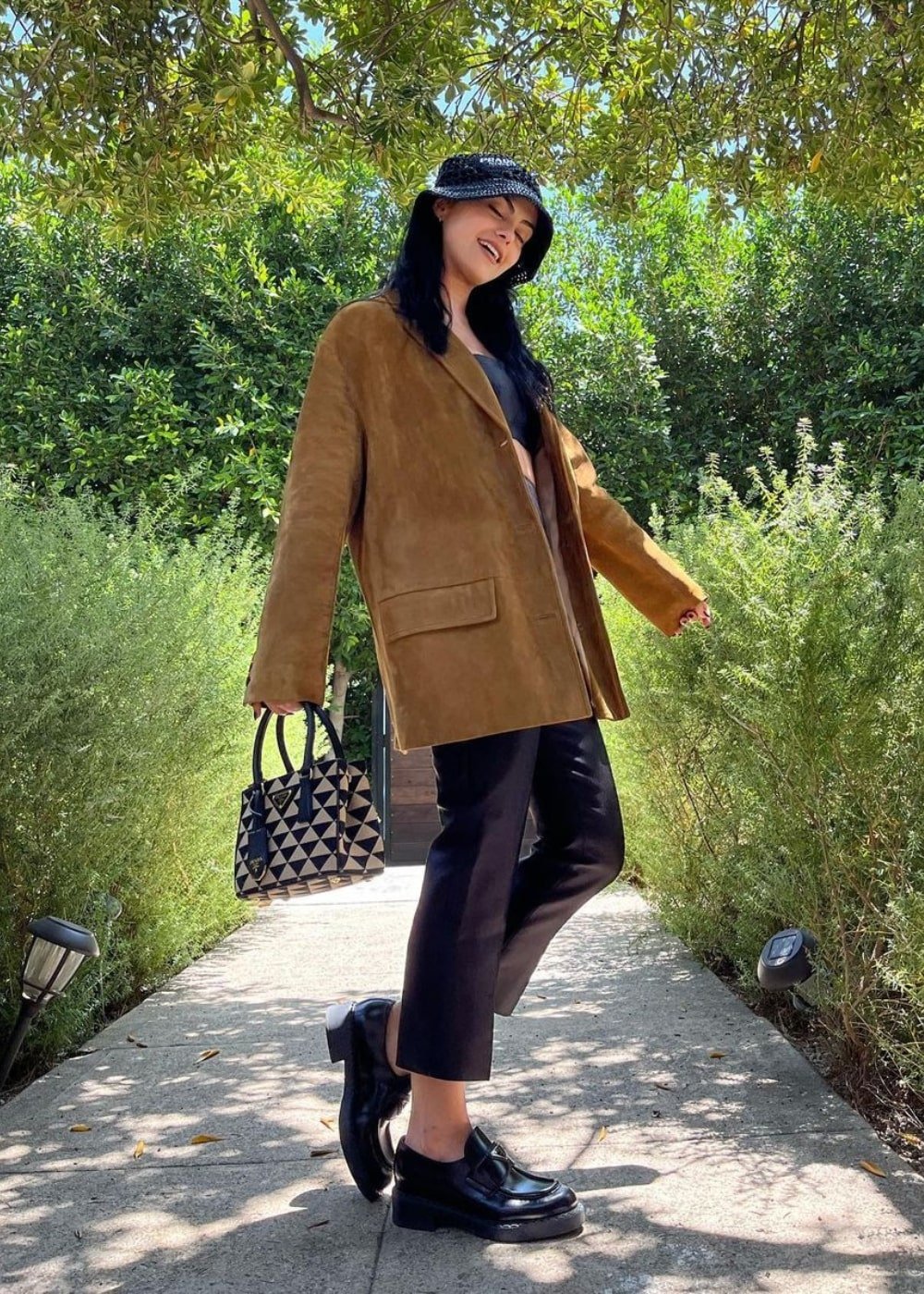 Camila Mendes - calça preta, top, casaco marrom, bucket hat e mocassim - Camila Mendes - Outono - em pé na rua - https://stealthelook.com.br