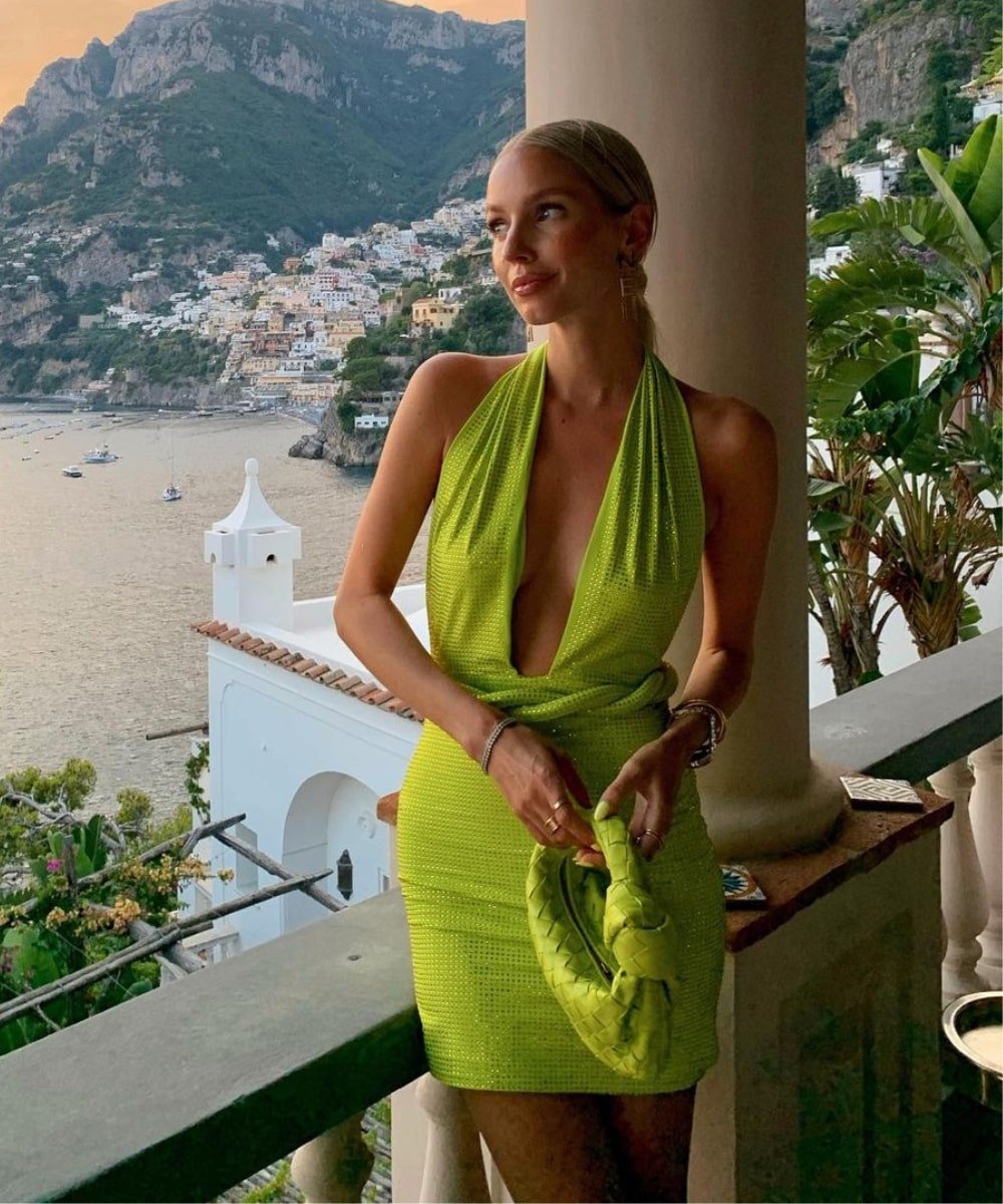 Leonie Hanne - vestido curto verde decotado - looks para casamento na praia - Verão - em pé em uma varanda segurando uma bolsa - https://stealthelook.com.br